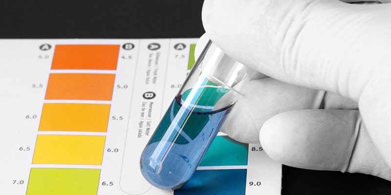 Person wearing gloves testing the PH of a chemical in a test tub